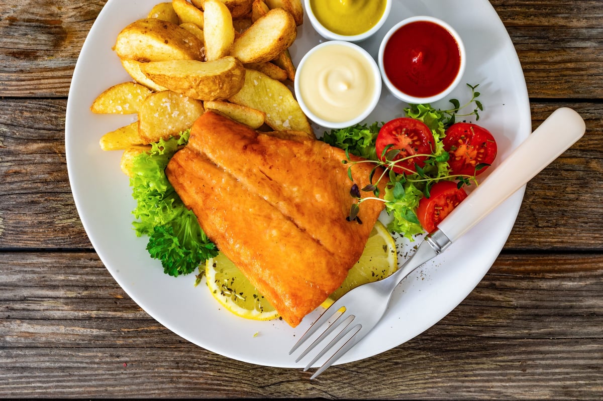 Fried salmon fillet with potato wedges and fresh salad on a wooden table