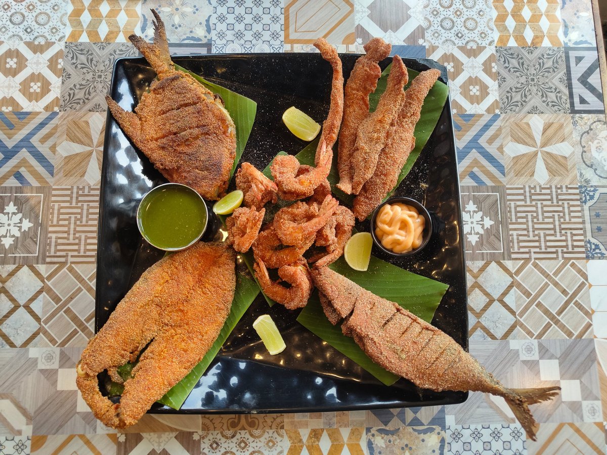 Golden crispy fried fish and prawns on a dark platter with lime wedges