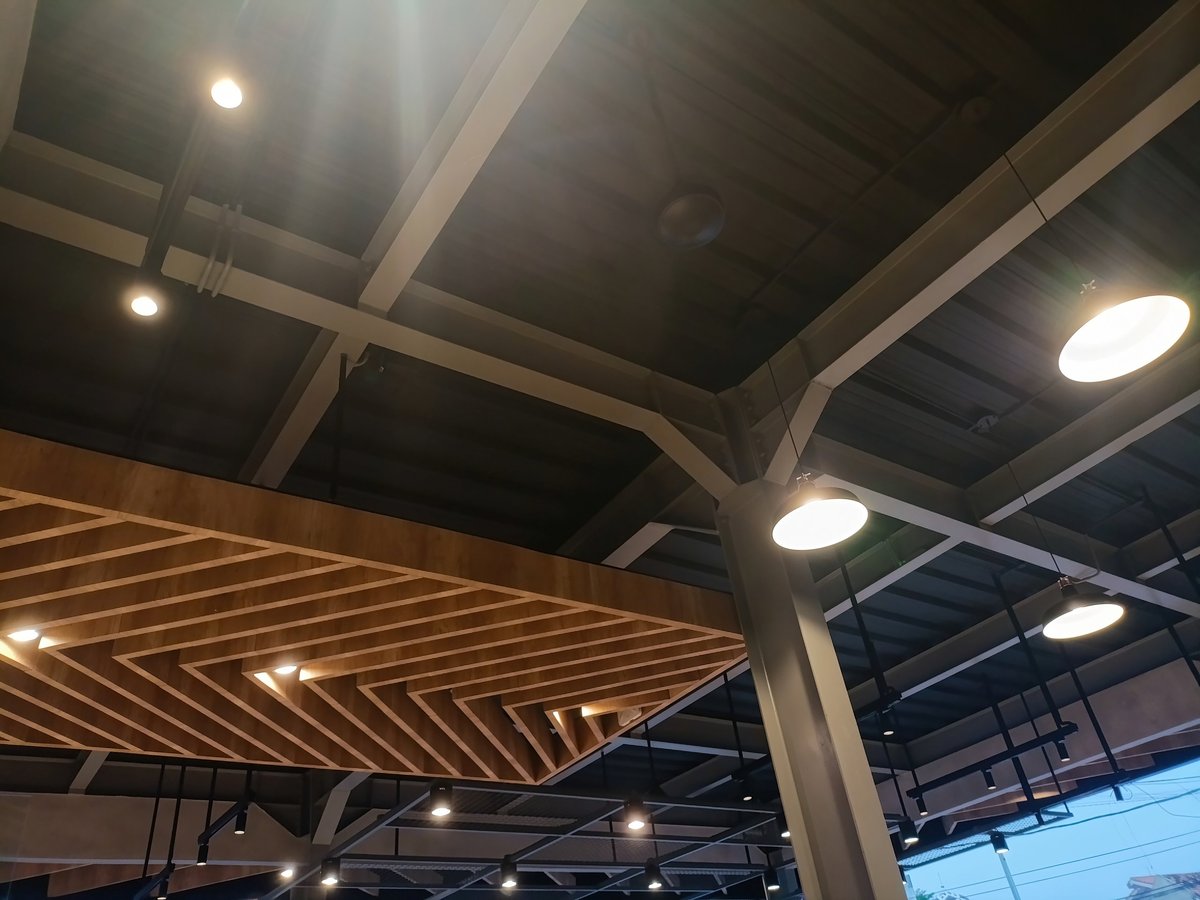 Warmly lit tavern ceiling with steel beams, wooden slats and hanging lamps